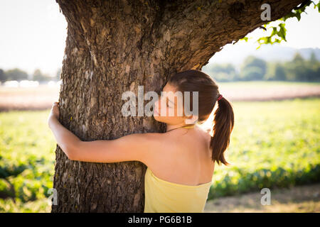 Mädchen umarmt Baum im Sommer Stockfoto