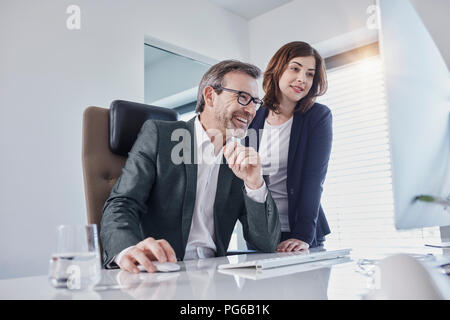 Lächelnd Geschäftsmann und geschäftsfrau am Computer am Schreibtisch im Büro suchen Stockfoto