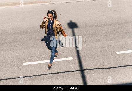 Junge Frau zu Fuß auf leere Straße, Kopfhörer tragen, Musik hören Stockfoto