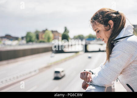 Sportliche junge Frau auf der Suche nach Uhr bei Autobahn Stockfoto