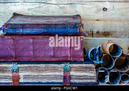 Stapel von drei alte Bücher auf einem Holzregal durch die Holzwand. Ein Stapel der alten Schriftrollen auf der rechten Seite der Bücher. Ein Bündel Stacheln in der Rol Stockfoto