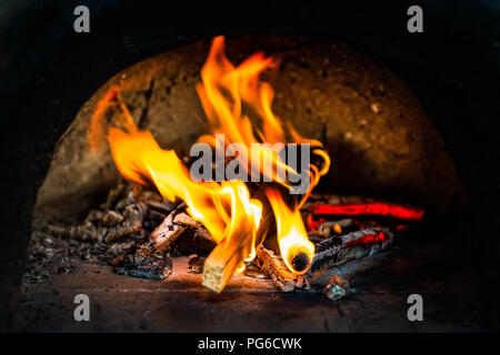 Brennholz brennt in einem kleinen Ofen aus Lehm. Feuer und Flamme, rote Glut, schwarze Asche. Detailansicht. Das Konzept der Wärme Stockfoto