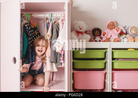 Ein kleines Mädchen sitzt in einem Schrank mit einer Abteilung. Storage System für Sachen für Kinder Stockfoto