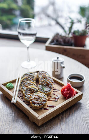 Gebackene Sushi und Rollen in eine hölzerne Platte mit Ingwer und Wasabi und Glas Weißwein Stockfoto