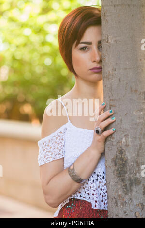 Junge Frau versteckt sich hinter Baum weg schauen Stockfoto