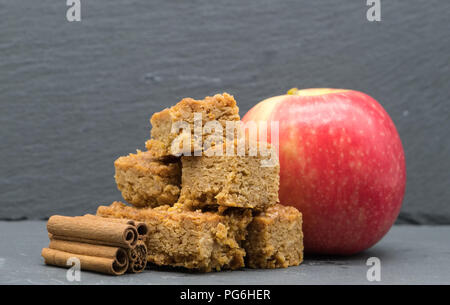 Bäcker Image mit flapjacks cinamon Sticks und einem roten Apfel auf der Rückseite des Bildes. Alle liegen auf Schiefer, wo der Schwerpunkt auf der Vorderseite Sharp ist dann d Stockfoto