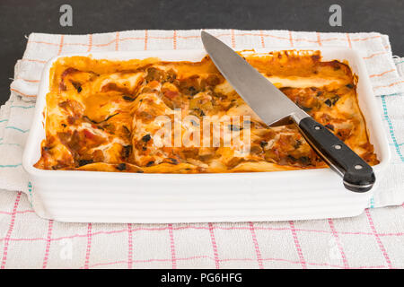 Eine vegetarische Lasagne gerade heraus Die ovan und bereit ist, mit den Köchen Messer liegen oben auf dem Teller zu schneiden. Stockfoto