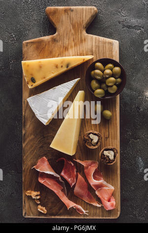 Flach mit verschiedenen Käse, Schinken und Oliven in Schale auf dunkle Oberfläche Stockfoto