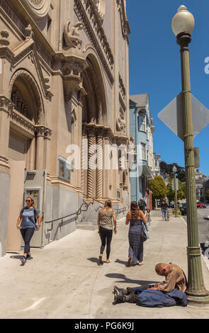 Obdachloser Mann schlief auf dem Bürgersteig durch den Mast, mit Fußgängern vorbei, in San Francisco, Kalifornien, USA. Stockfoto