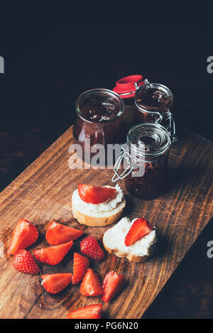 Ansicht von Sandwiches mit Frischkäse, Erdbeere Schichten und Konfitüre auf Schneidebrett auf Schwarz Stockfoto