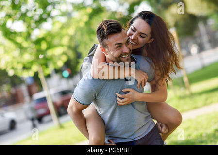 Glücklicher Mann geben Freundin eine Huckepack Fahrt im park Stockfoto