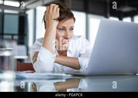 Frustrierte geschäftsfrau am Glas Tisch sitzen im Büro am Laptop suchen Stockfoto