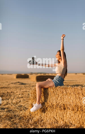 Junge Frau sitzt auf Strohballen unter selfie mit Instant Kamera Stockfoto