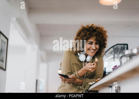 Junge Frau mit Kopfhörer in Coworking Space, pausieren, Kuchen essen Stockfoto