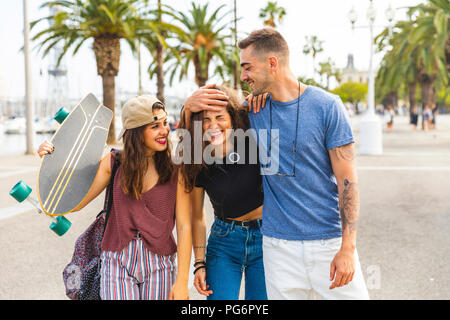 Gerne Freunde mit einem Skateboard gehen auf eine Strandpromenade mit Palmen Stockfoto