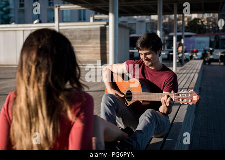 Lächelnd Mann sitzt auf einer Bank, Gitarre spielen für Freundin Stockfoto