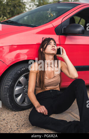 Junge Frau sitzt am Straßenrand mit einer Autopanne Aufruf Pannenhilfe Stockfoto