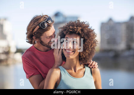 Glückliches junges Paar, Mann flüsternd ins Ohr der Frau Stockfoto