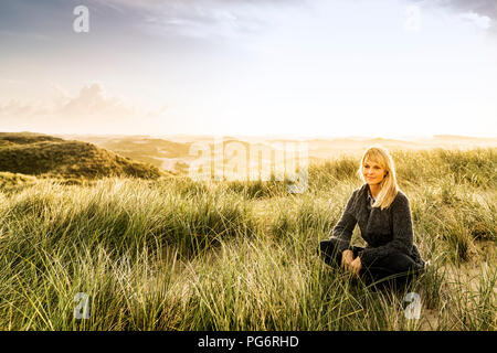 Lächelnde Frau in den Dünen sitzen Stockfoto