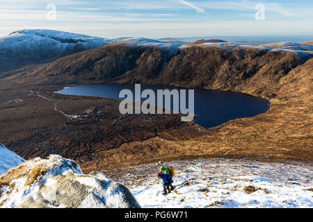 Zwei hillwalkers steilen Boden in Schnee auf Doan Berg in Richtung Lough Shannagh mit Carn Berg und Slieve Dreck hinter sich. Stockfoto