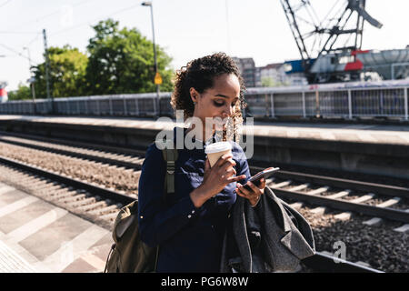 Junge Frau am Bahnhof Lesen von SMS-Nachrichten auf Ihrem Handy Stockfoto