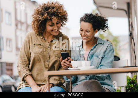 Zwei Freunde, die in Coworking Space, am Tisch sitzend mit Kaffee, mit Smartphone Stockfoto