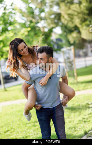 Glücklicher Mann geben Freundin eine Huckepack Fahrt im park Stockfoto