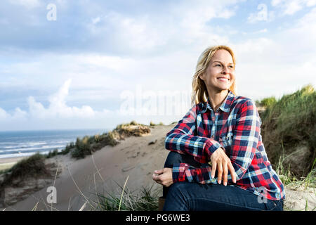 Lächelnde Frau in den Dünen sitzen Stockfoto