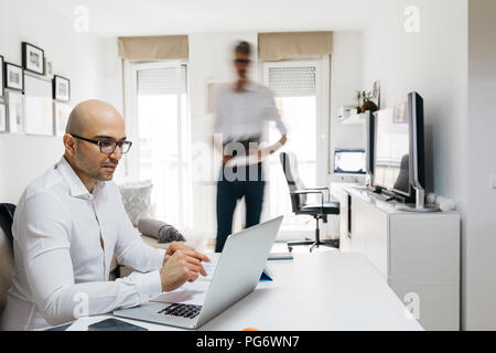 Mann mit Laptop im Home Office mit Kollege bewegte Vergangenheit Stockfoto