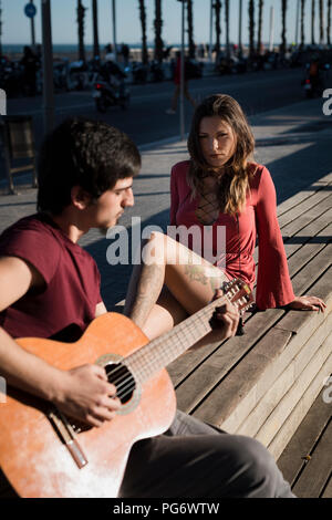 Spanien, Barcelona, Paar mit einer Gitarre sitzen auf einer Bank an der Strandpromenade Stockfoto