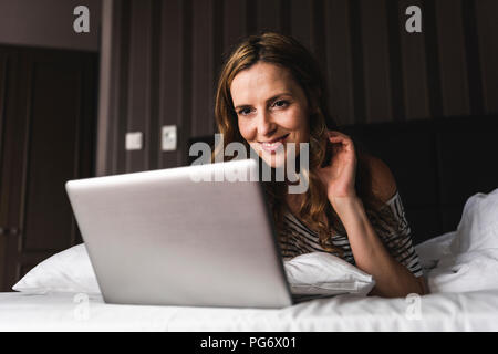 Lächelnde Frau liegend auf Bett zu Hause am Laptop suchen Stockfoto