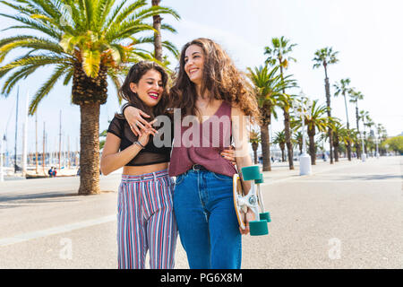 Glückliche junge Frau und ein junges Mädchen mit einem Skateboard auf einer Strandpromenade mit Palmen Stockfoto