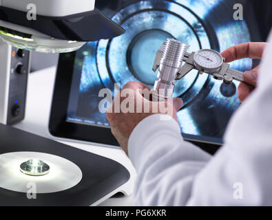 Ingenieur mit Messschieber und ein 3D-Stereo Mikroskop für die Qualitätskontrolle in der Herstellung von technischen Komponenten für die Industrie Stockfoto