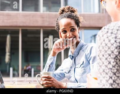 Junge Kolleginnen und Kollegen draußen sitzen, zusammen arbeiten, mit Mittagessen Stockfoto