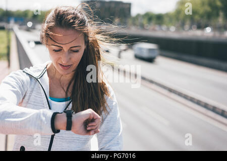 Sportliche junge Frau auf der Suche nach Uhr bei Autobahn Stockfoto