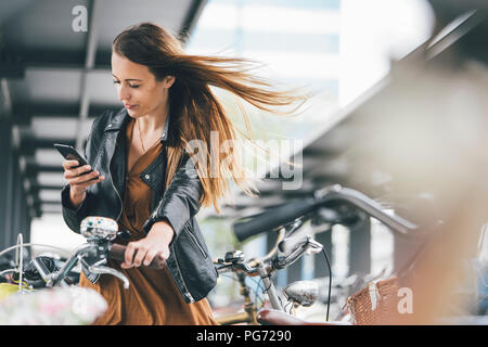 Junge Frau mit Fahrrad über Handy in der Stadt
