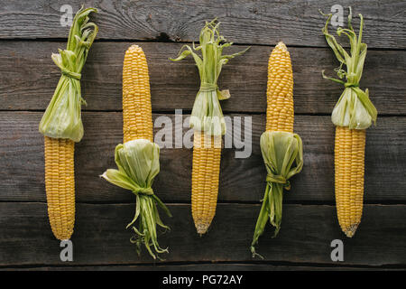 Flach mit Anordnung der raw Maiskolben auf hölzernen Tischplatte Stockfoto