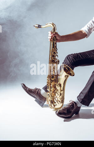 7/8 shot professioneller junger Musiker mit Saxophon auf Grau Stockfoto