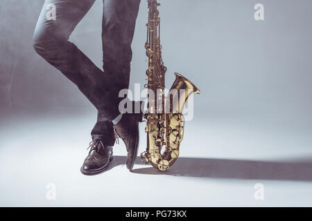 Niedrige Abschnitt der professionellen Musiker mit Saxophon in Rauch auf Grau Stockfoto