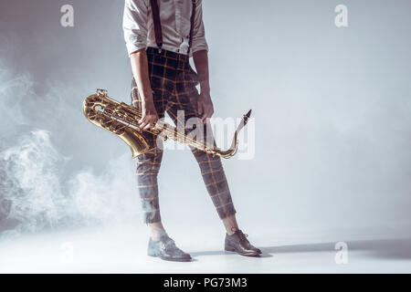 7/8 Schuß von stilvollen junge Musiker mit Saxophon in Rauch auf Grau Stockfoto