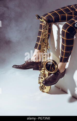 Niedrige Abschnitt der professionellen Musiker mit Saxophon in Rauch auf Grau Stockfoto
