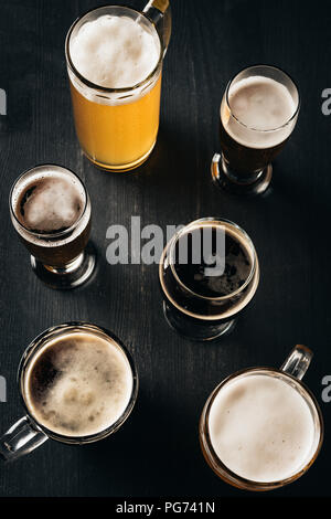 Blick von oben auf die Anordnung der Gläser kaltes Bier auf dunklen, hölzernen Tischplatte Stockfoto