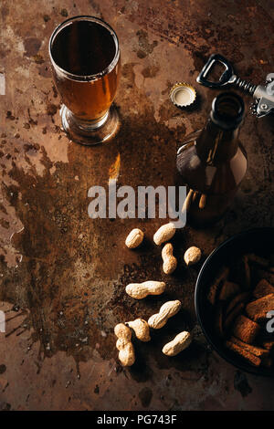 Ansicht von oben angeordnet, Erdnüsse, gebackenem Brot, Flasche und Glas Bier auf Rost Tischplatte Stockfoto