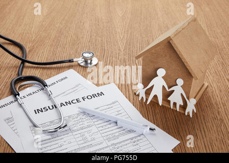 - Aus der Nähe ansehen der Versicherung, Versicherung Gesundheit Antragsformular, Stift, Stethoskop, Haus Modell und Papier schneiden Familie auf hölzernen Tisch Stockfoto