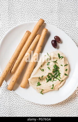 Blick von oben auf die Hummus, Grissini und Oliven auf Teller auf Leinen Stockfoto