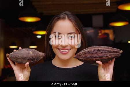 BANOS, Ecuador, August, 17, 2018: in der Nähe von schönen Frau Holding in den Händen zwei Stücke von cacao Topf und das Tragen schwarzer Kleidung Stockfoto