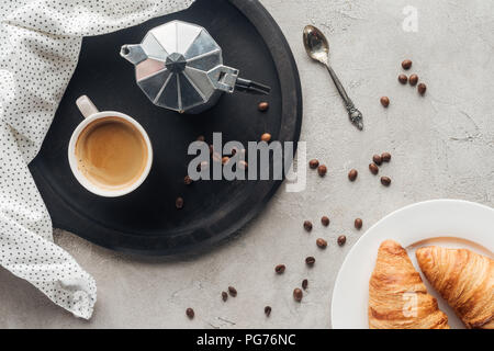 Blick von oben auf die Tasse Kaffee und moka Topf auf die Betonoberfläche mit verschüttetem Kaffee Bohnen und die Platte von Croissants Stockfoto