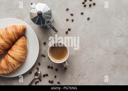 Blick von oben auf die Tasse Kaffee mit Gipfeli und moka Topf auf die Betonoberfläche mit verschüttetem Kaffee Bohnen Stockfoto