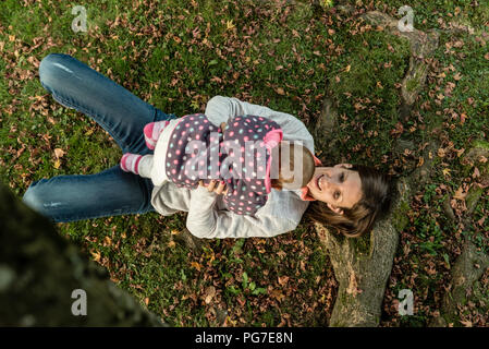 Luftaufnahme der glücklichen Mutter spielt mit ihrem Baby Girl auf dem Gras unter Blätter im Herbst. Stockfoto