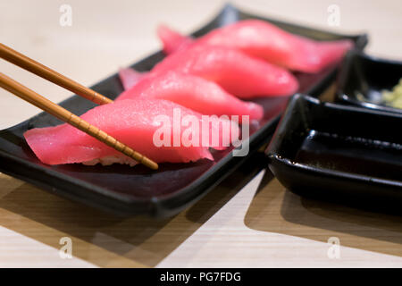 Vier Thunfisch Sushi mit Stäbchen in schwarz Platte auf dem Tisch im japanischen Restaurant. Stockfoto